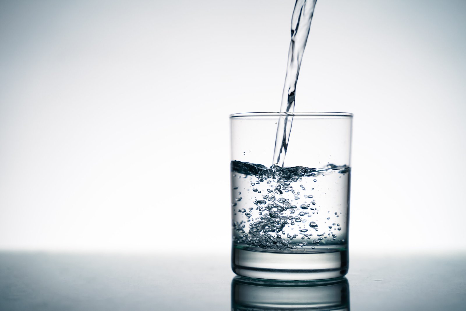 Close up of pouring fresh water into the clear glass from the bottle on table.